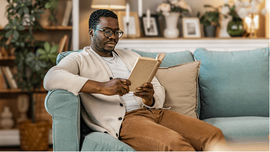 Pessoa sentada confortavelmente em um sofá, lendo um livro